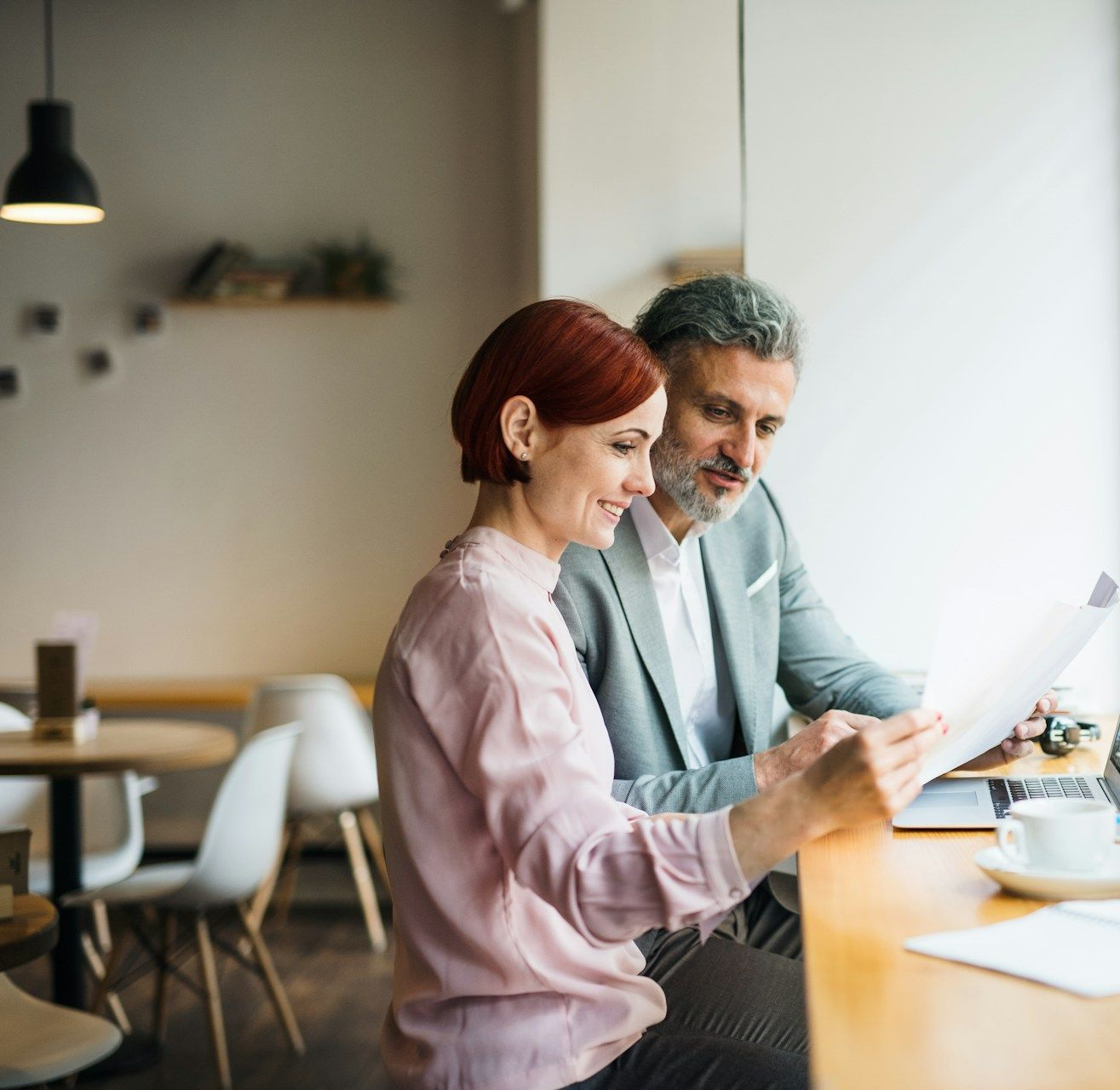 Woman in glasses on the phone, smiling, looking at papers, wearing a patterned blazer.