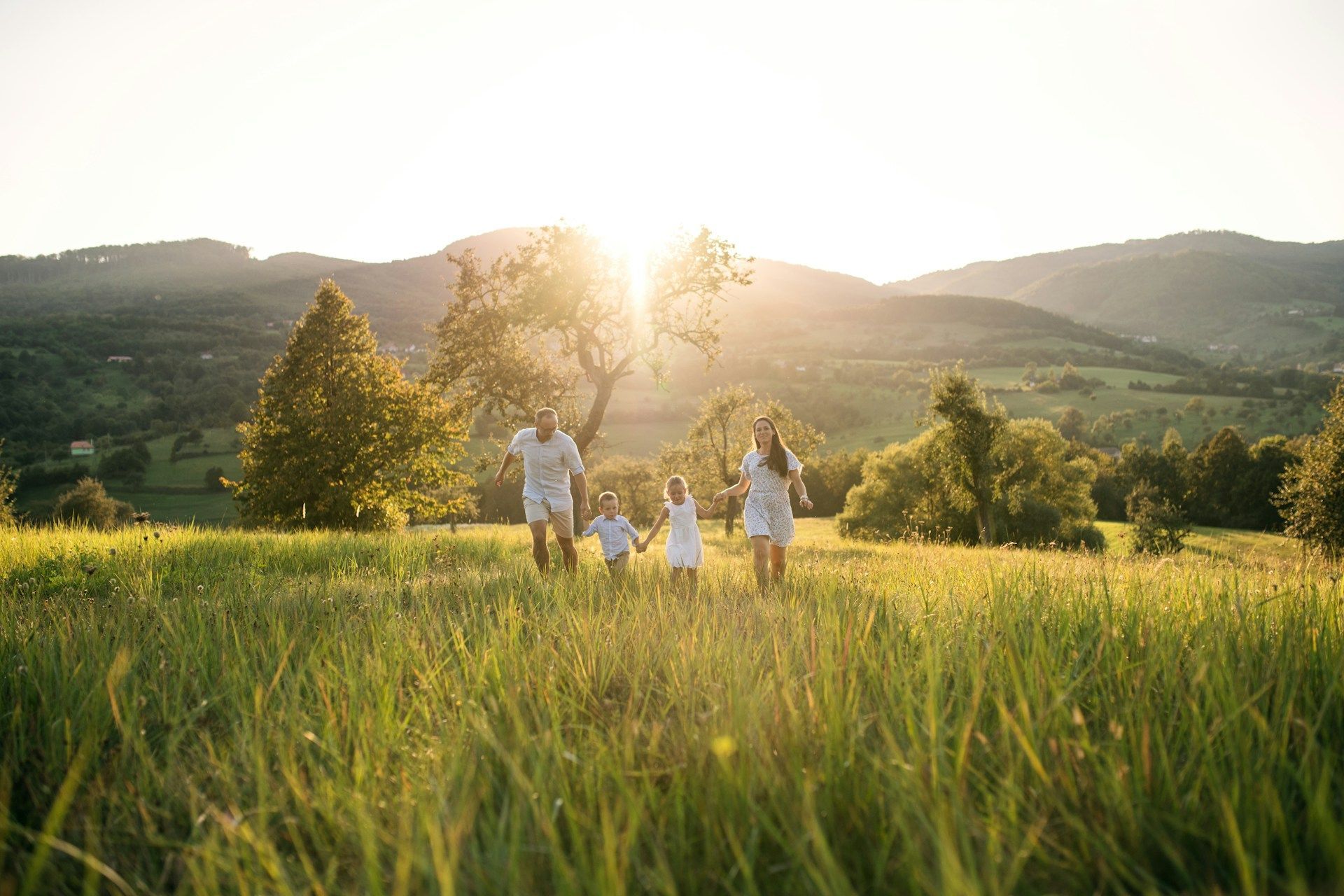 A family holds hands while running through a grassy field at sunset with mountains in the background.