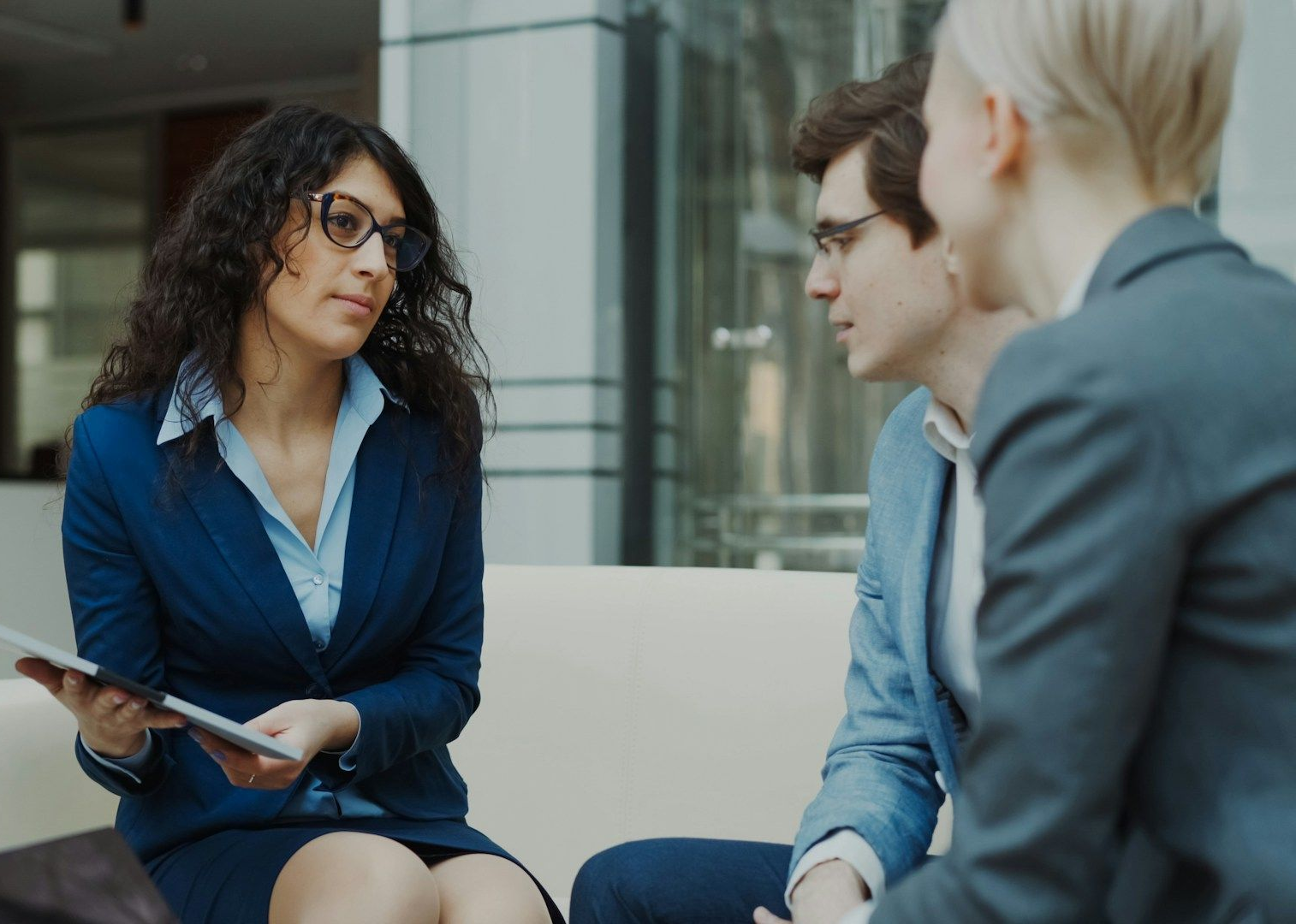 Woman in glasses on the phone, smiling, looking at papers, wearing a patterned blazer.