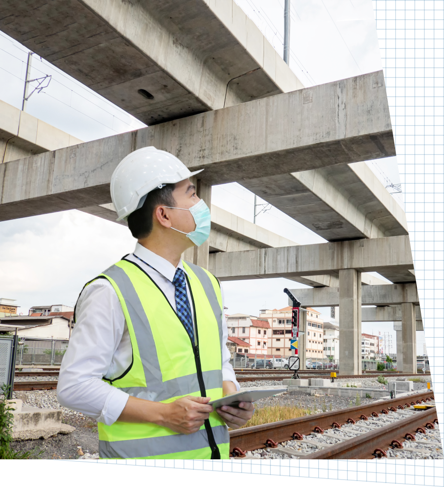 A man wearing a hard hat and safety vest is standing under a bridge.