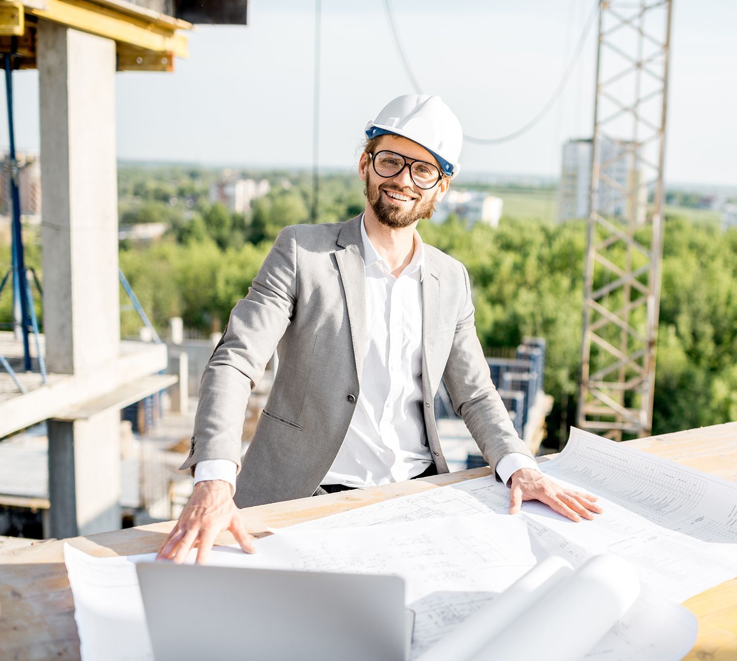 A man in a suit and hard hat is standing next to a laptop on a construction site. A man in a suit and hard hat is standing next to a laptop on a construction site.
