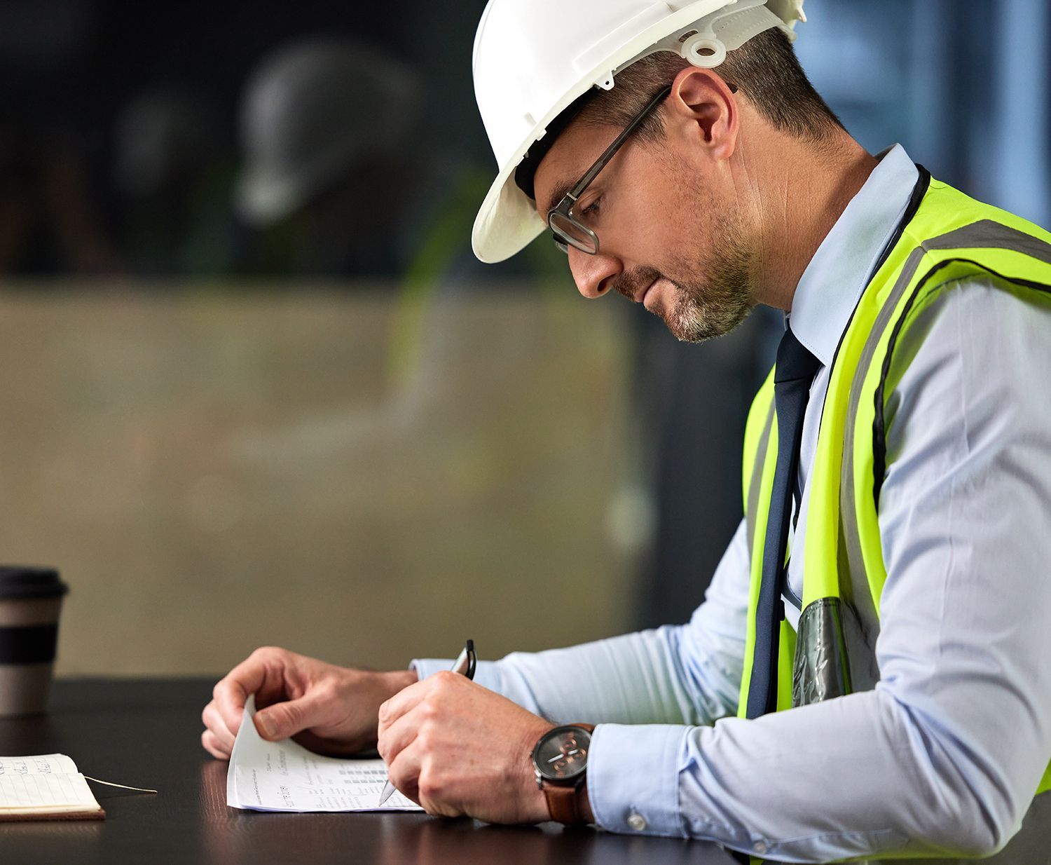 A man wearing a hard hat and safety vest is writing on a piece of paper. A man wearing a hard hat and safety vest is writing on a piece of paper.