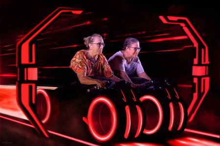 Two people seated in a glowing red futuristic cockpit, facing forward with focused expressions