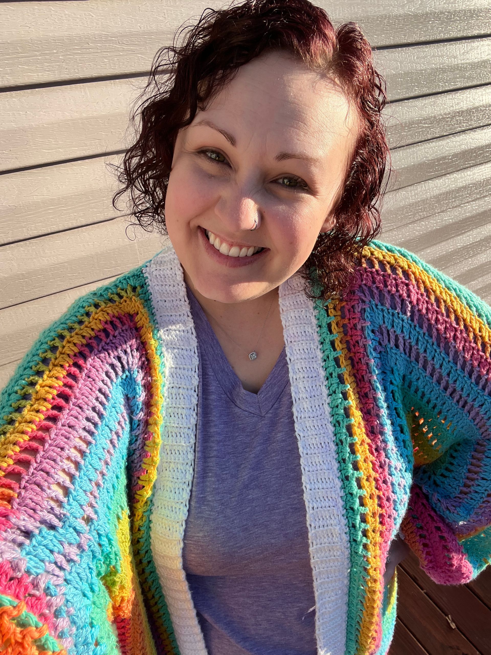 Woman smiling, wearing a rainbow crocheted cardigan.