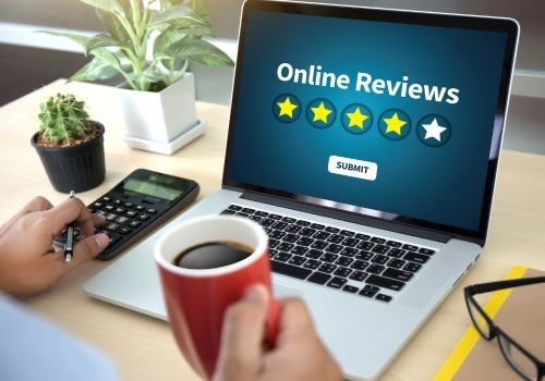 Laptop displaying online reviews, with a hand holding a coffee cup and using a calculator.