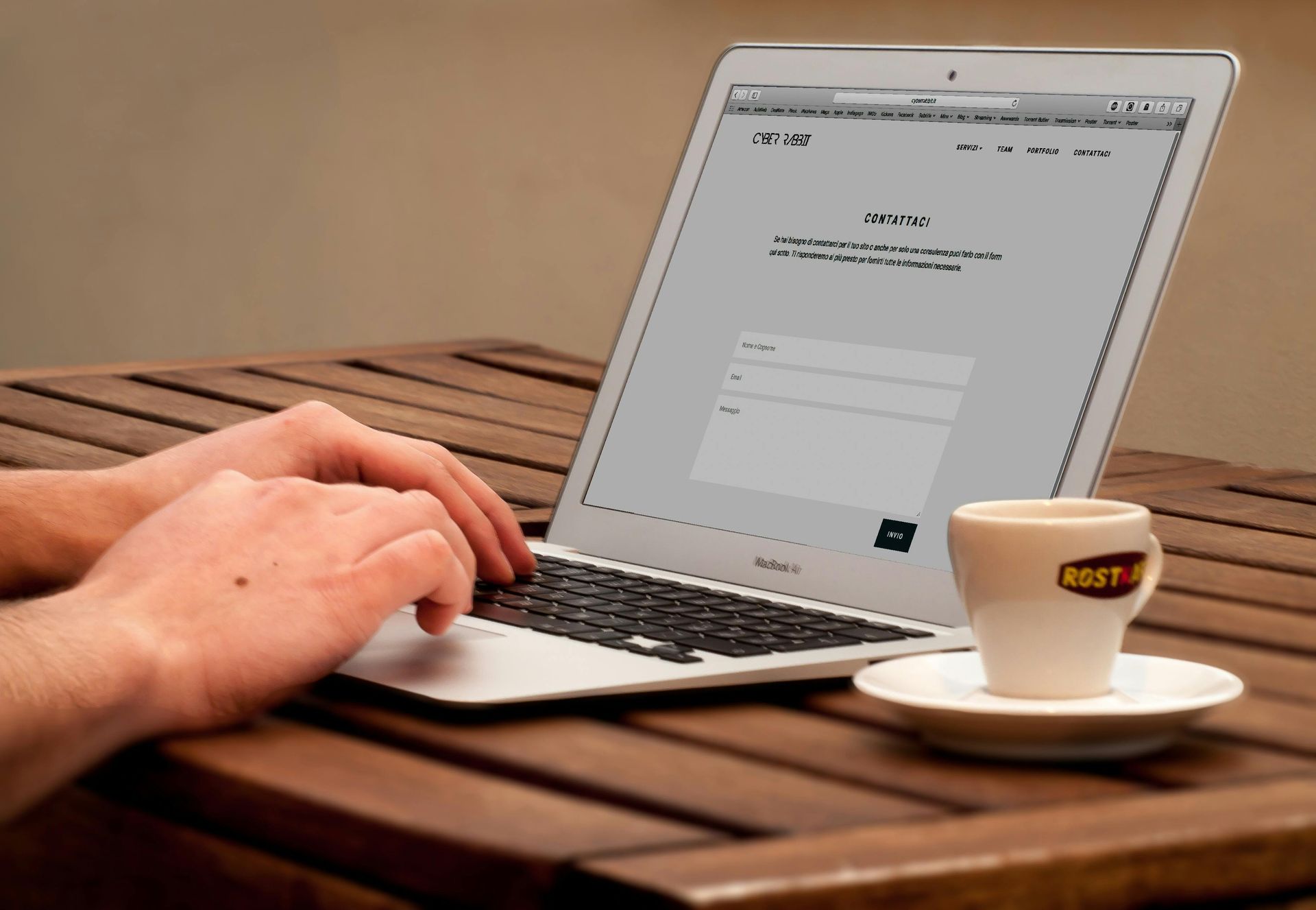 Person typing on a laptop on a wooden table, next to a cup of coffee.