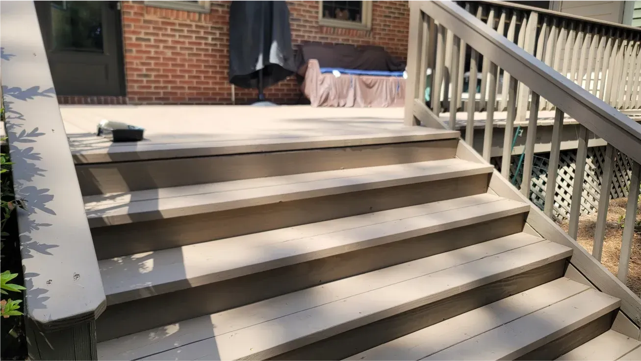 A set of stairs leading up to a deck with a brick building in the background.