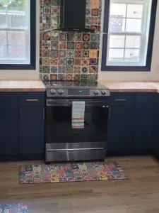 A kitchen with a stove and a rug on the floor.