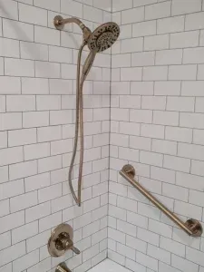 A shower with a hand rail and a shower head on a white brick wall.