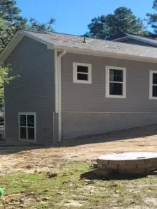 A gray house with white trim and windows is sitting on top of a dirt hill.