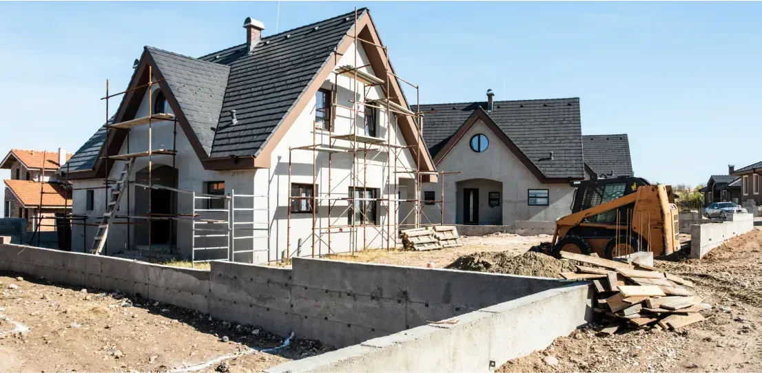 A house is being built in a residential area with a bulldozer in the background.