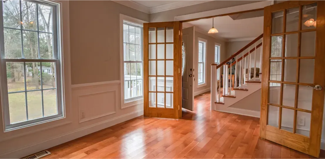 An empty living room with hardwood floors and french doors leading to the stairs.