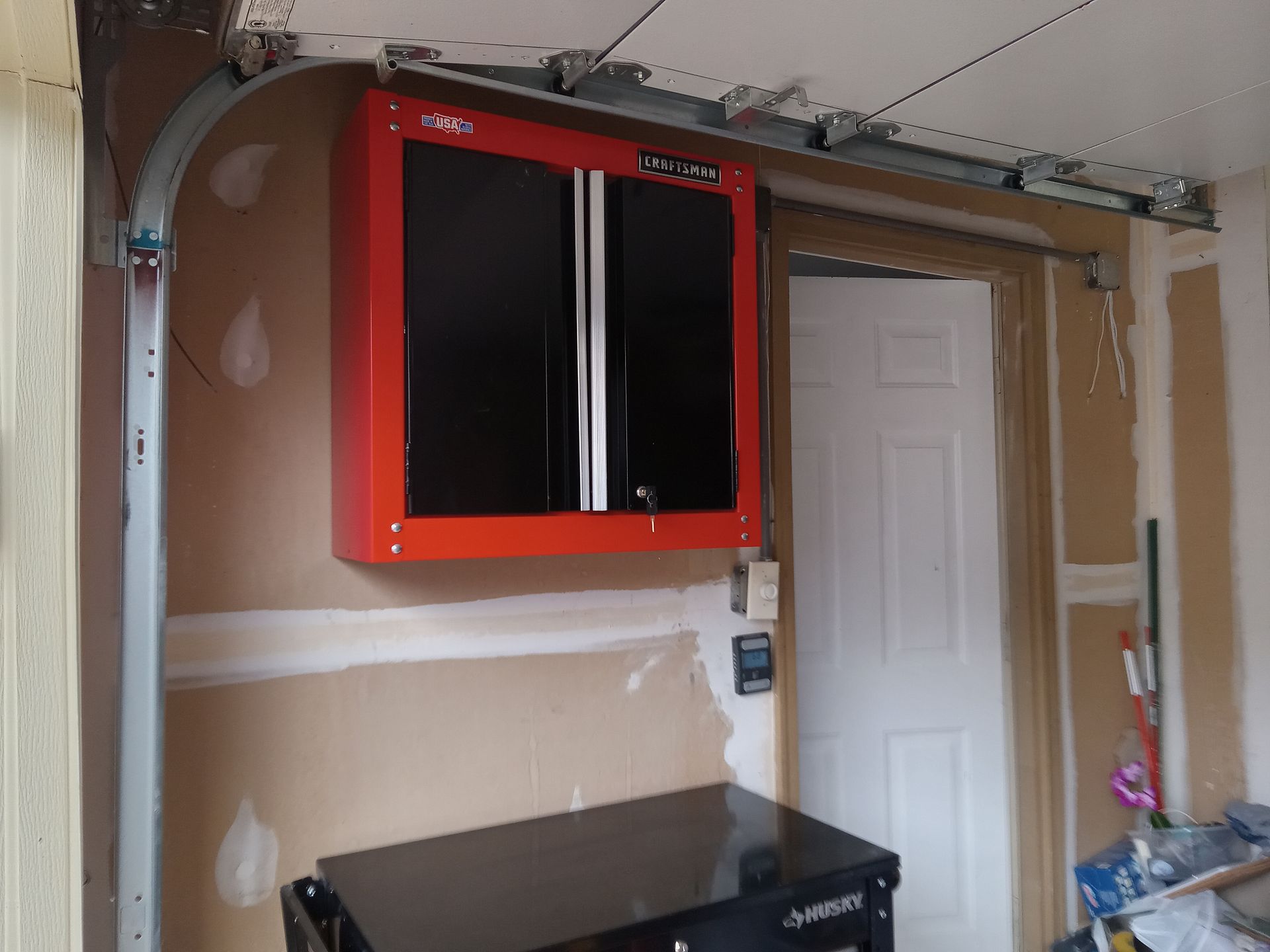 A red cabinet is hanging above a black cabinet in a garage.