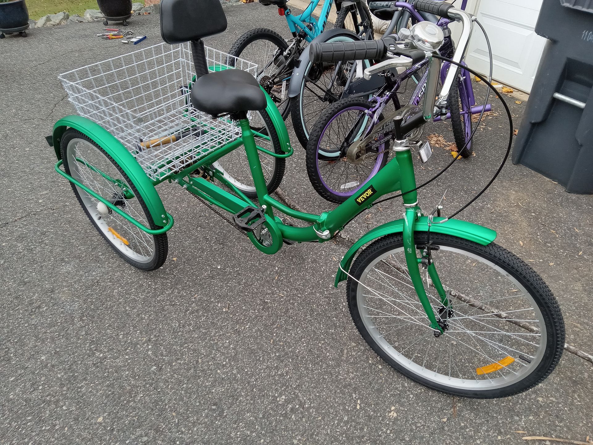 A green tricycle with a basket is parked next to other bicycles.