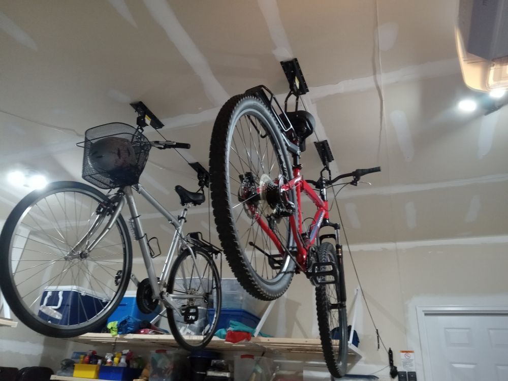Two bicycles are hanging from the ceiling in a garage.
