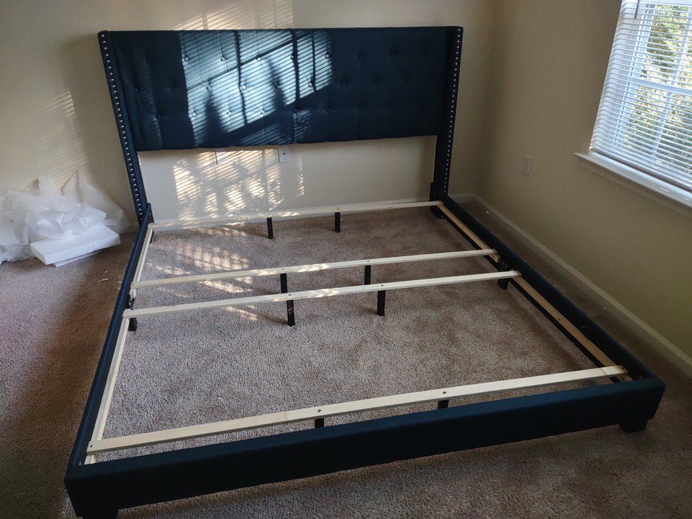 A bed frame is sitting in a bedroom next to a window.