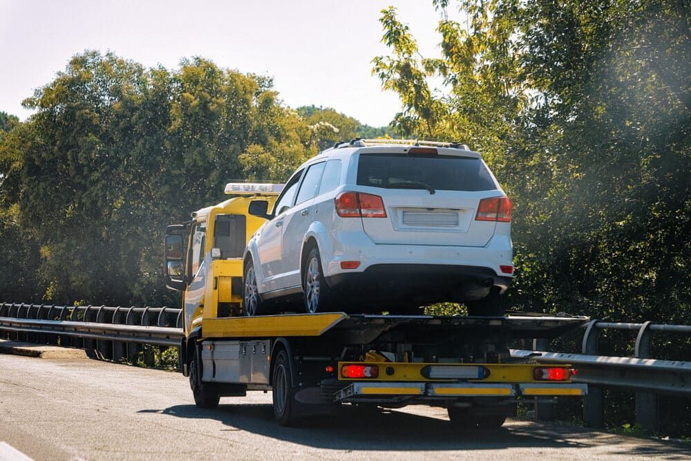 A White Suv Is Being Towed by A Tow Truck on A Highway — Multidrive Parts Australia in Armidale, NSW