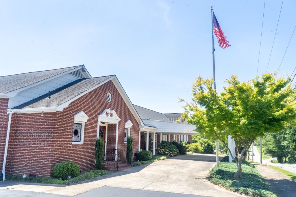 Brick building with American flag waving, driveway, and tree in front.