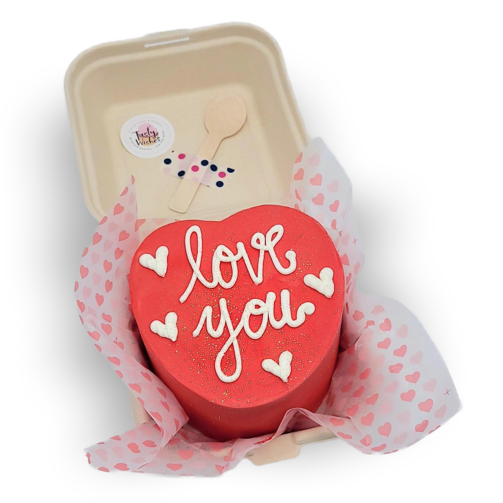 A heart-shaped red bento cake decorated with white icing that says 