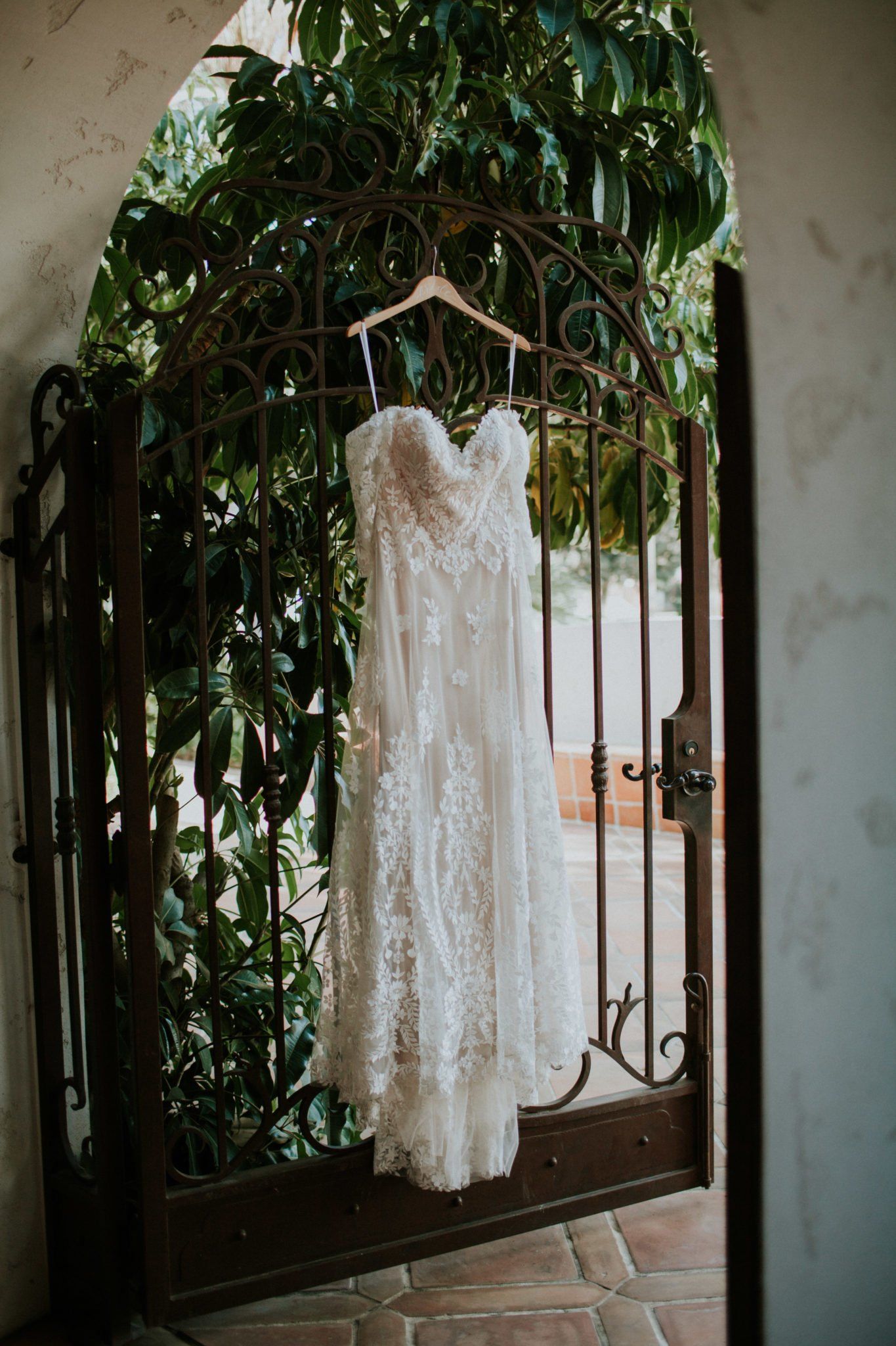 A wedding dress is hanging on a hanger in front of a gate.