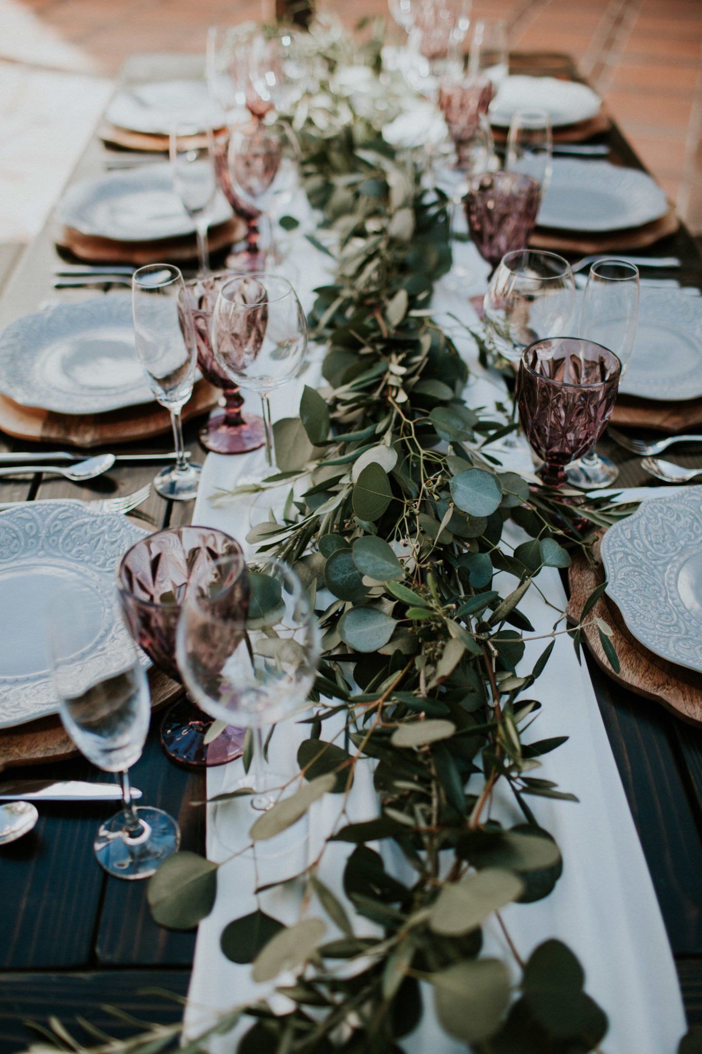 A long table with plates , glasses , and a table runner.