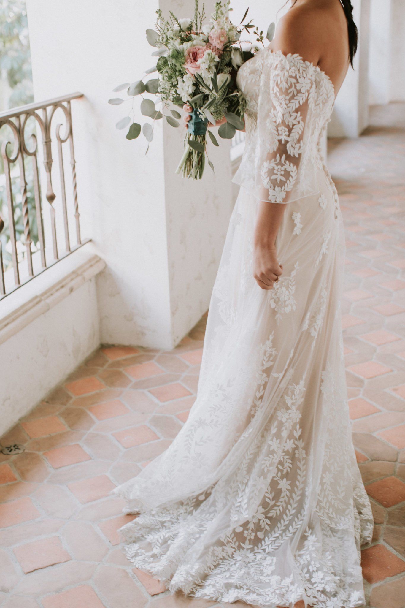 A bride in a white lace wedding dress is holding a bouquet of flowers.
