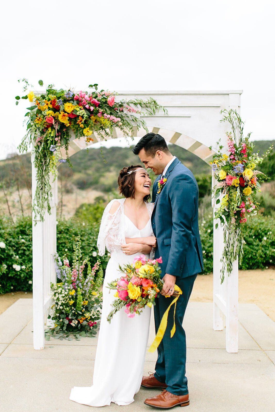 A bride and groom are standing under an arch decorated with flowers.