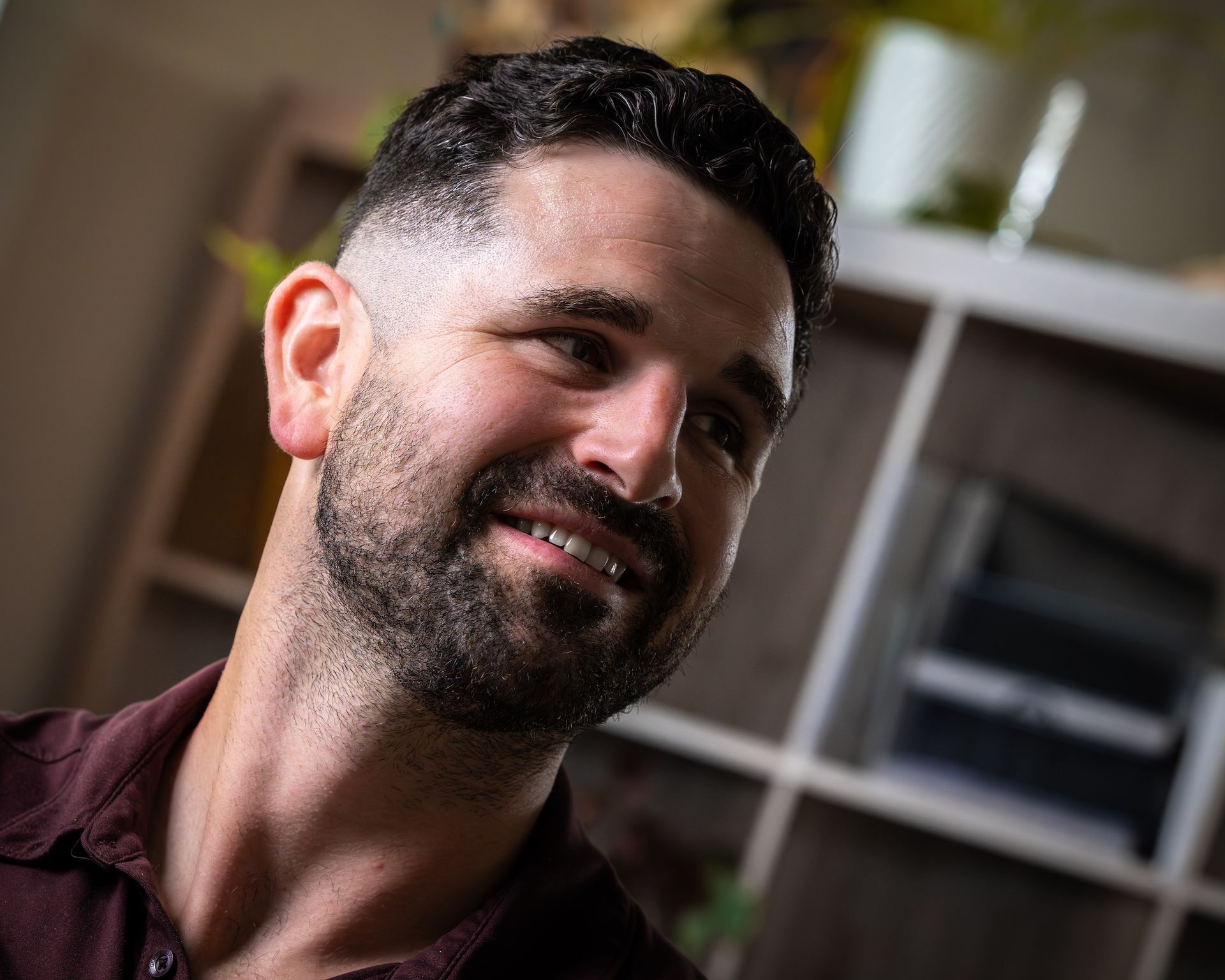 A man with a beard is smiling in front of a bookshelf.