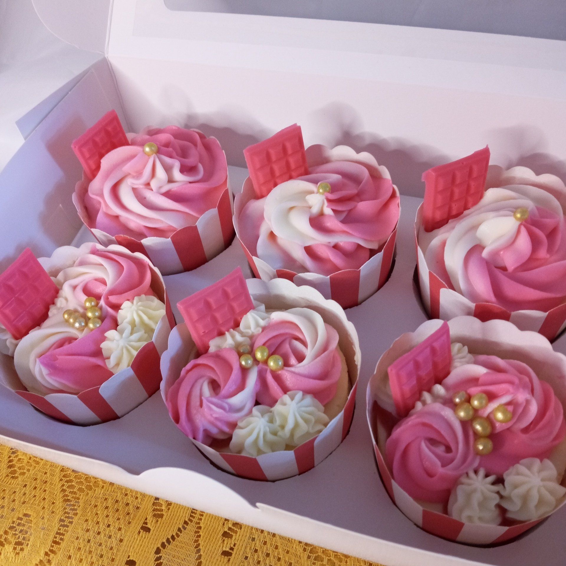 Six pink and white cupcakes are in a box