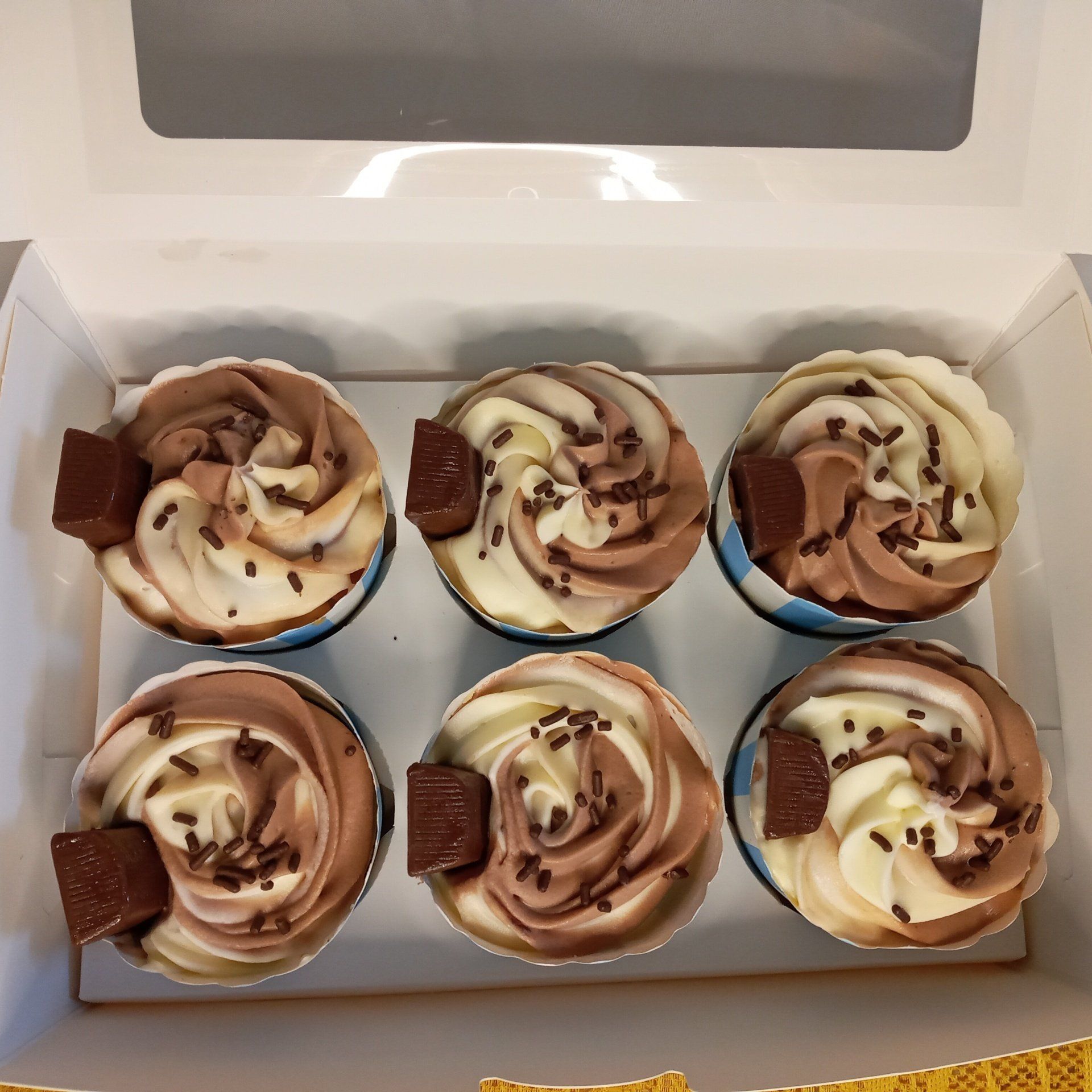 Six cupcakes with chocolate frosting and sprinkles in a box