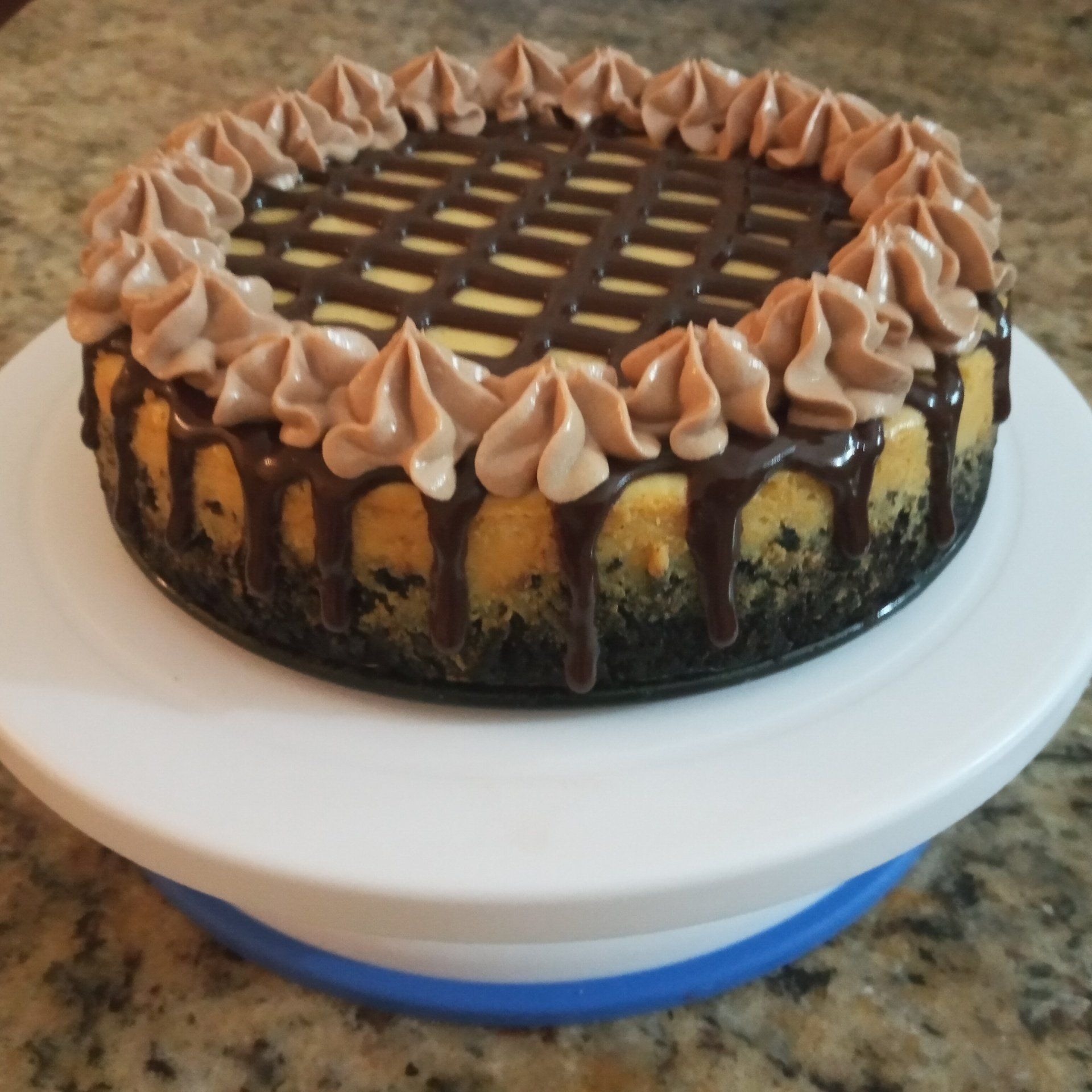 A cheesecake with chocolate frosting sits on a turntable