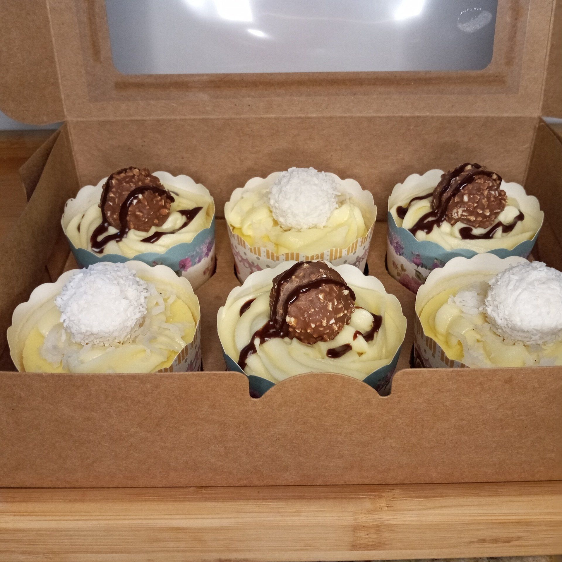 A box of cupcakes with coconut and chocolate on top