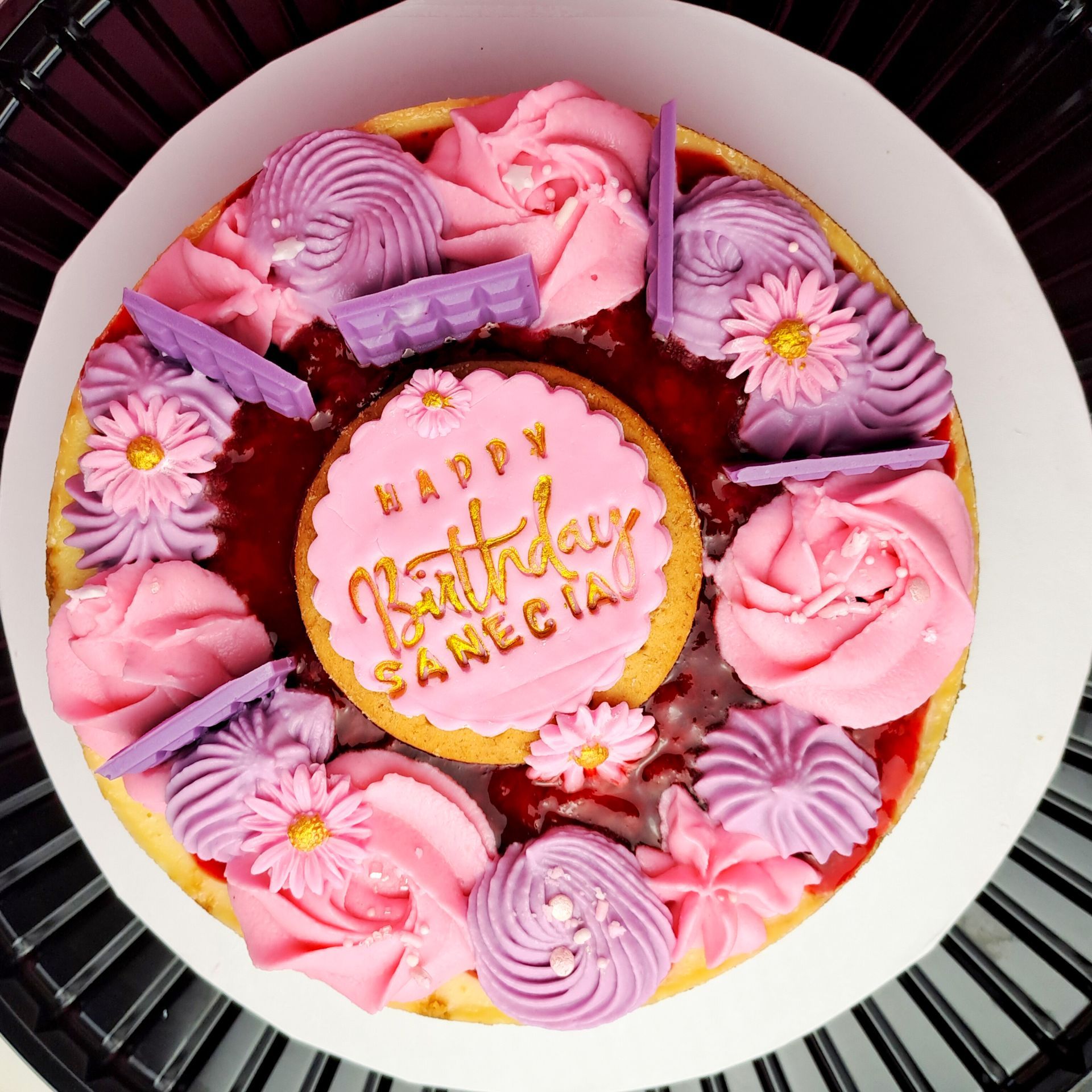 A birthday cake with pink and purple frosting and flowers
