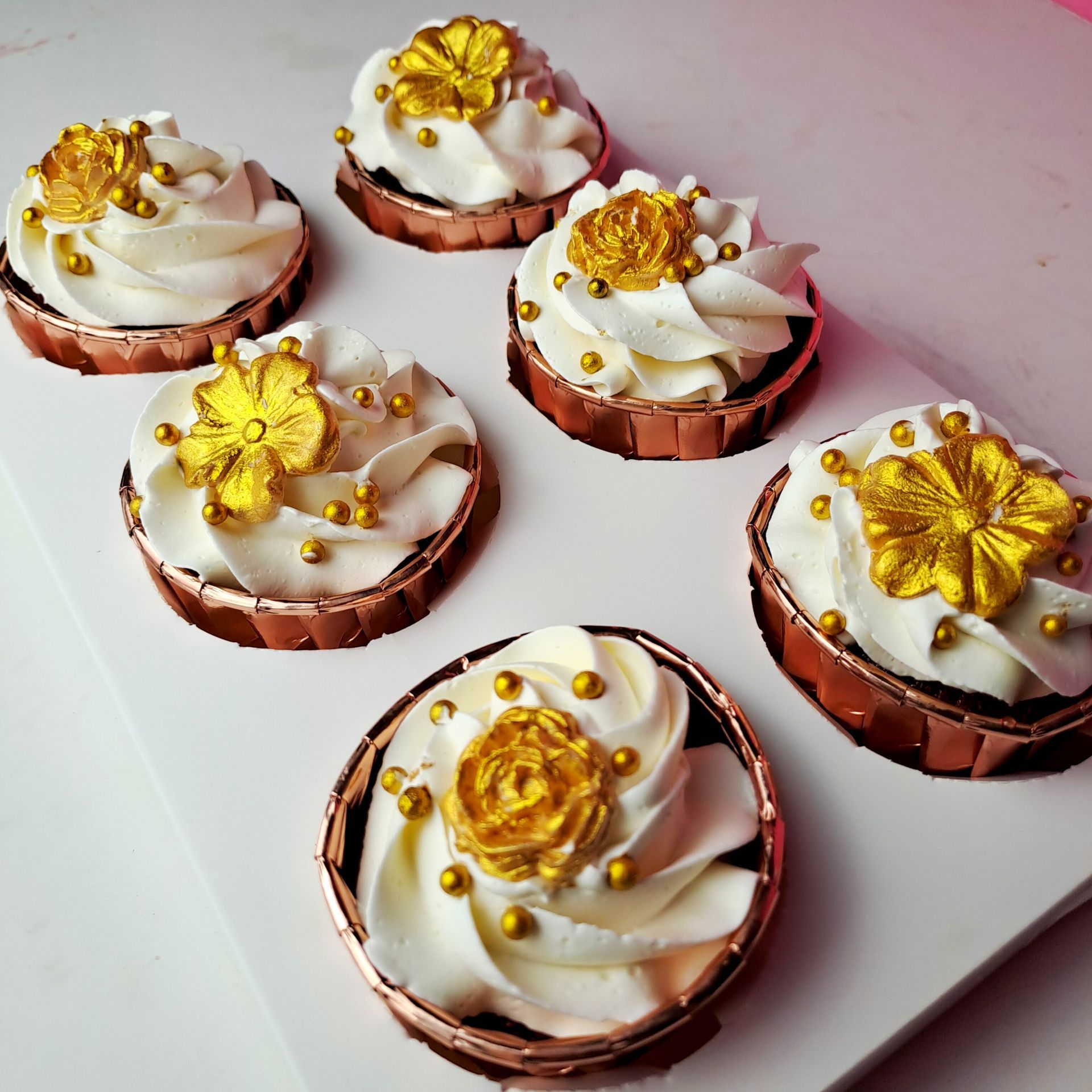 A tray of cupcakes with white frosting and gold flowers