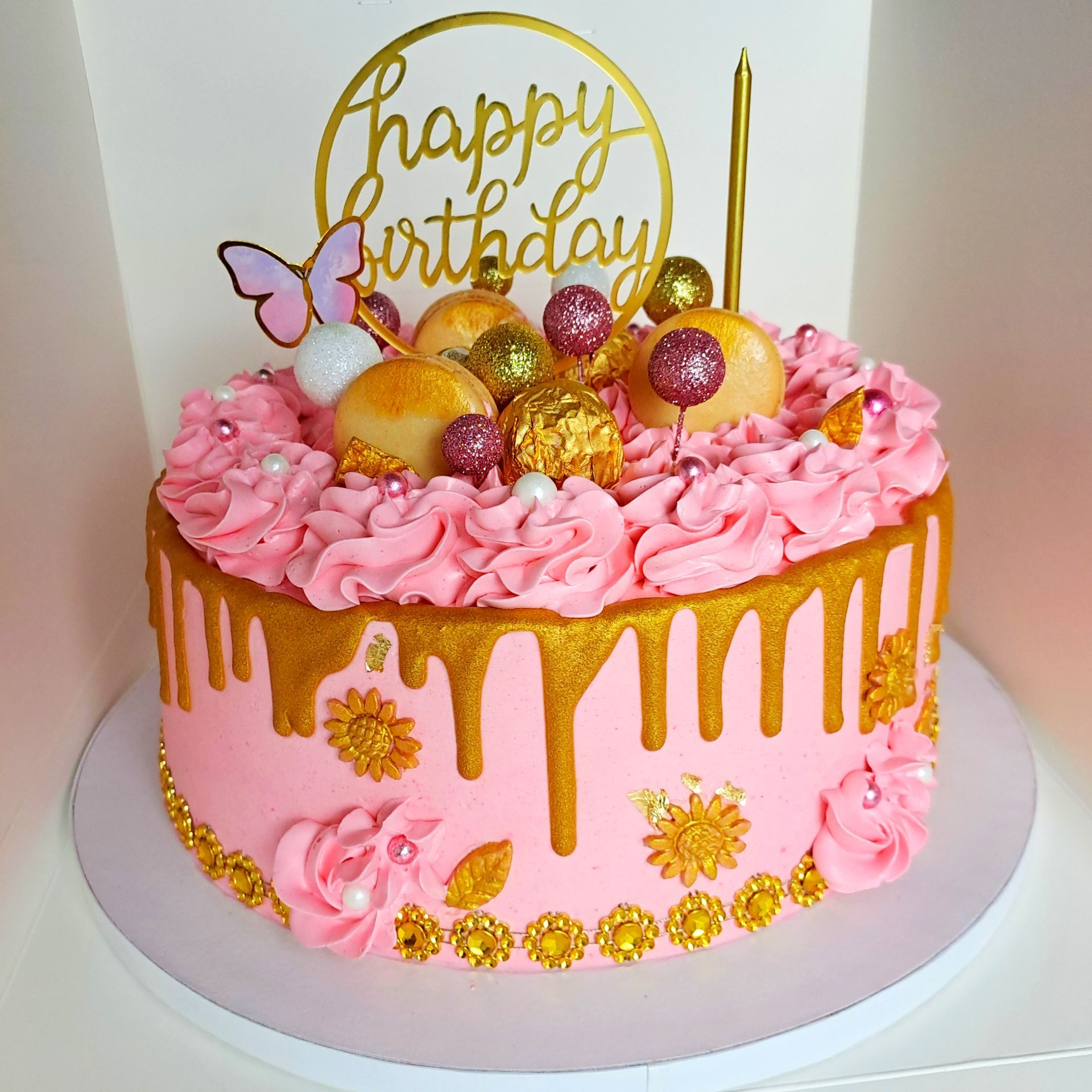 A pink and gold birthday cake with a happy birthday topper