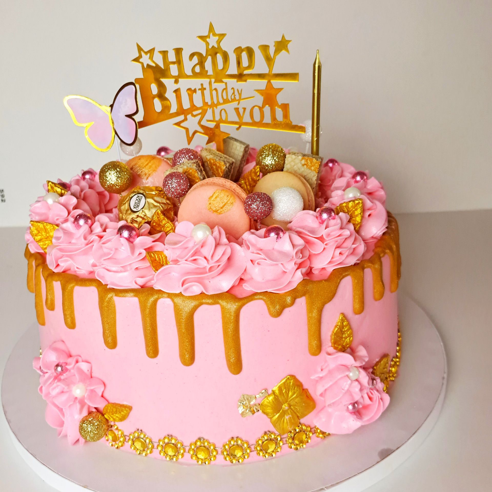 A pink and gold birthday cake with a happy birthday topper