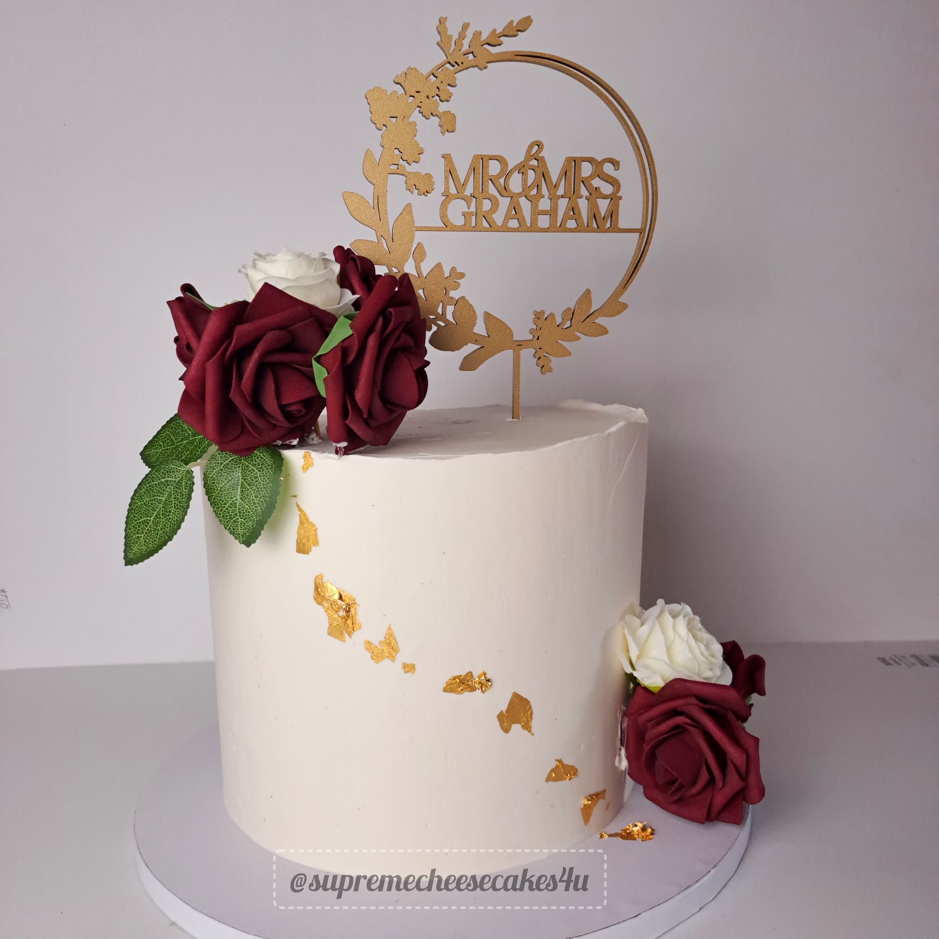 A white cake with red roses and a topper that says mr and mrs graham