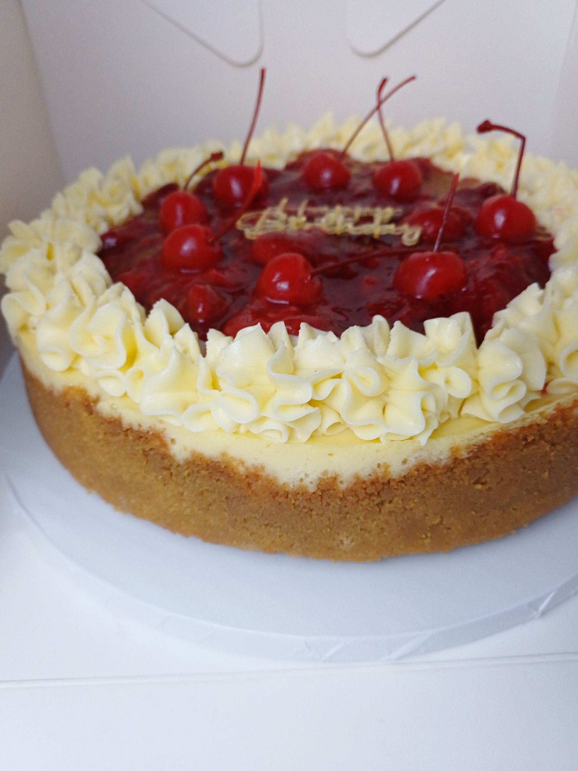 A cherry cheesecake with a graham cracker crust and piped cream border, topped with maraschino cherries.