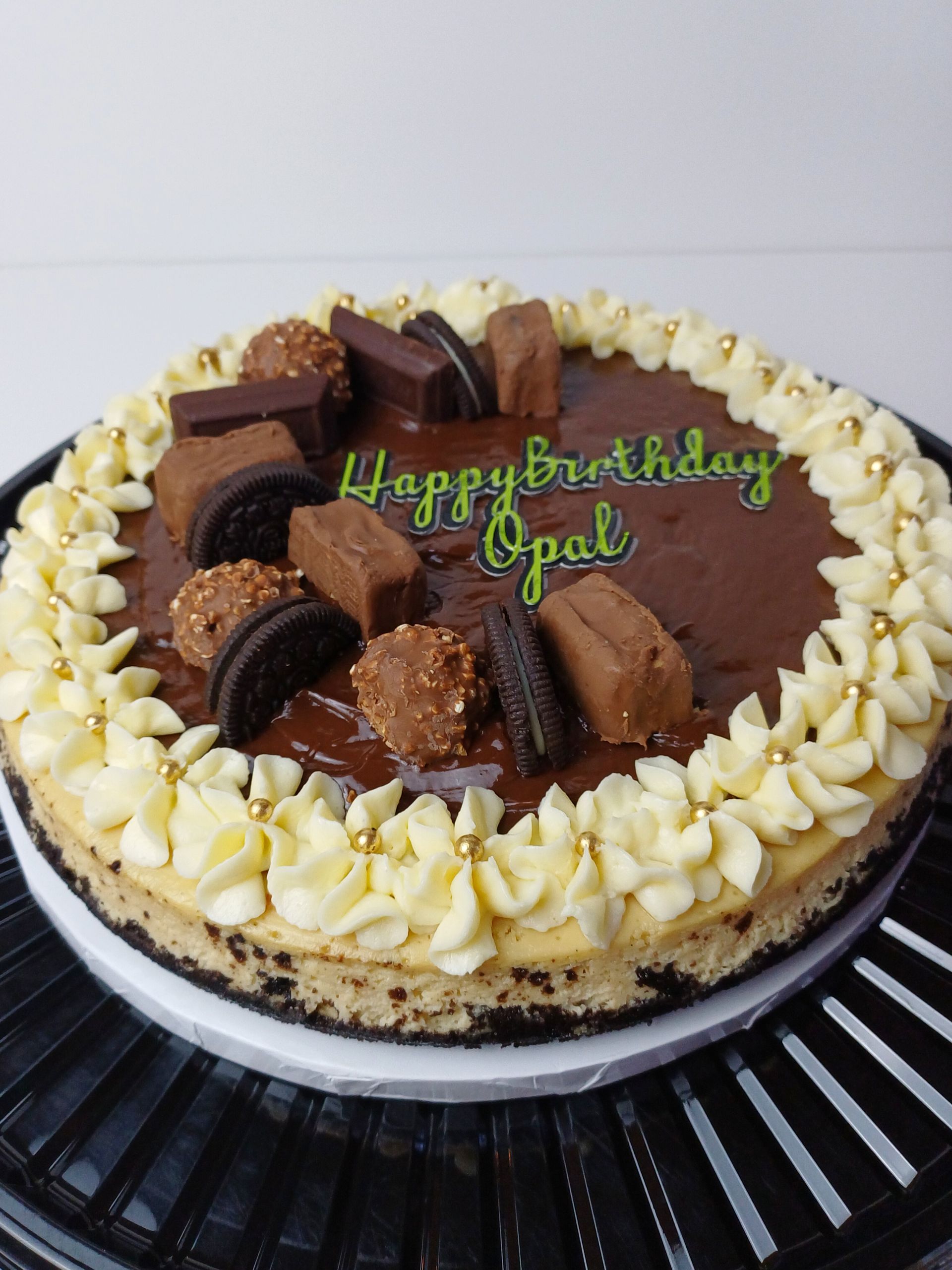 A cheesecake topped with chocolate ganache, various chocolates, and piped frosting with 