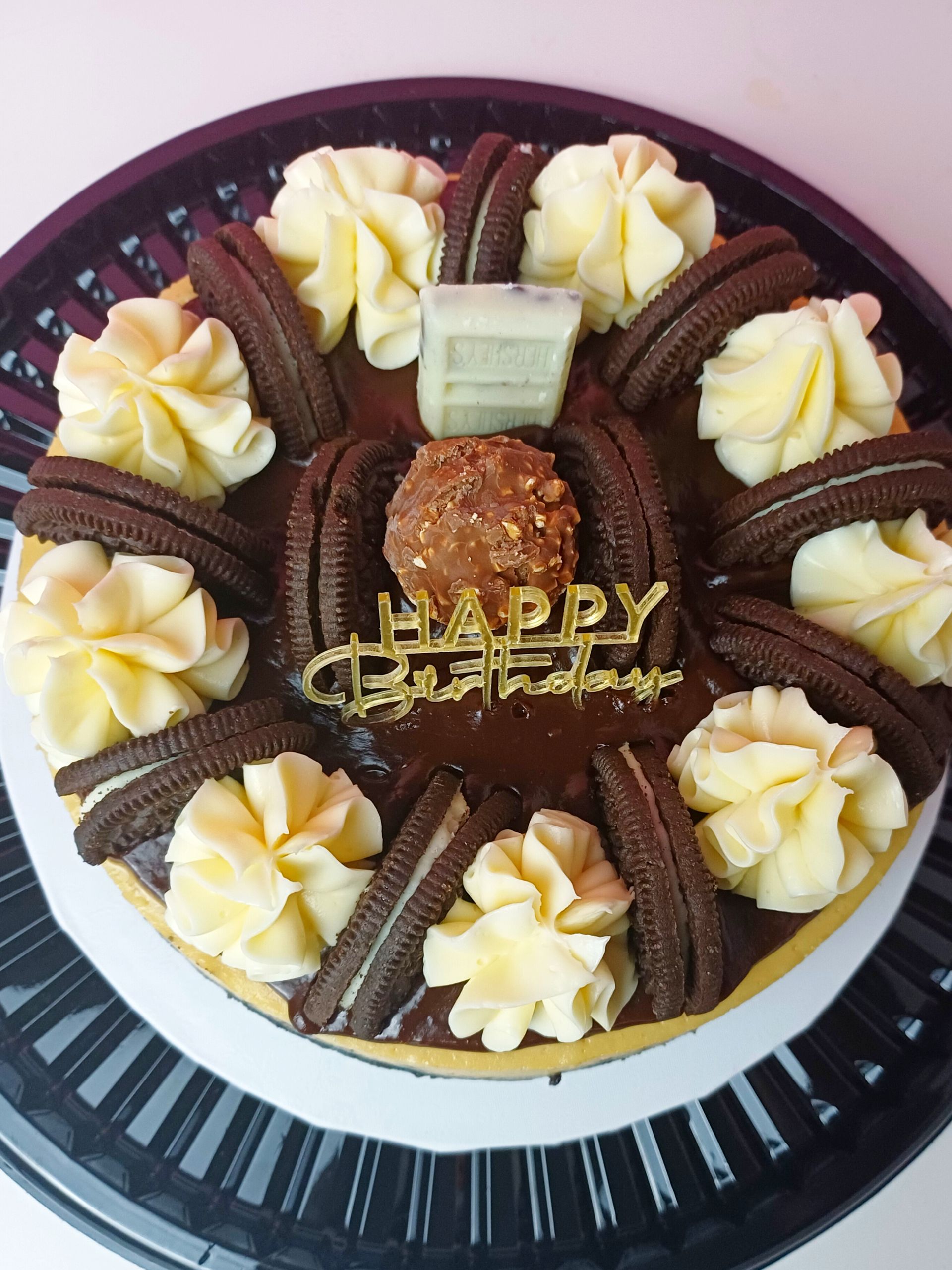 A chocolate birthday cake decorated with piped frosting swirls, Oreo cookies, a Ferrero Rocher, and a gold topper.