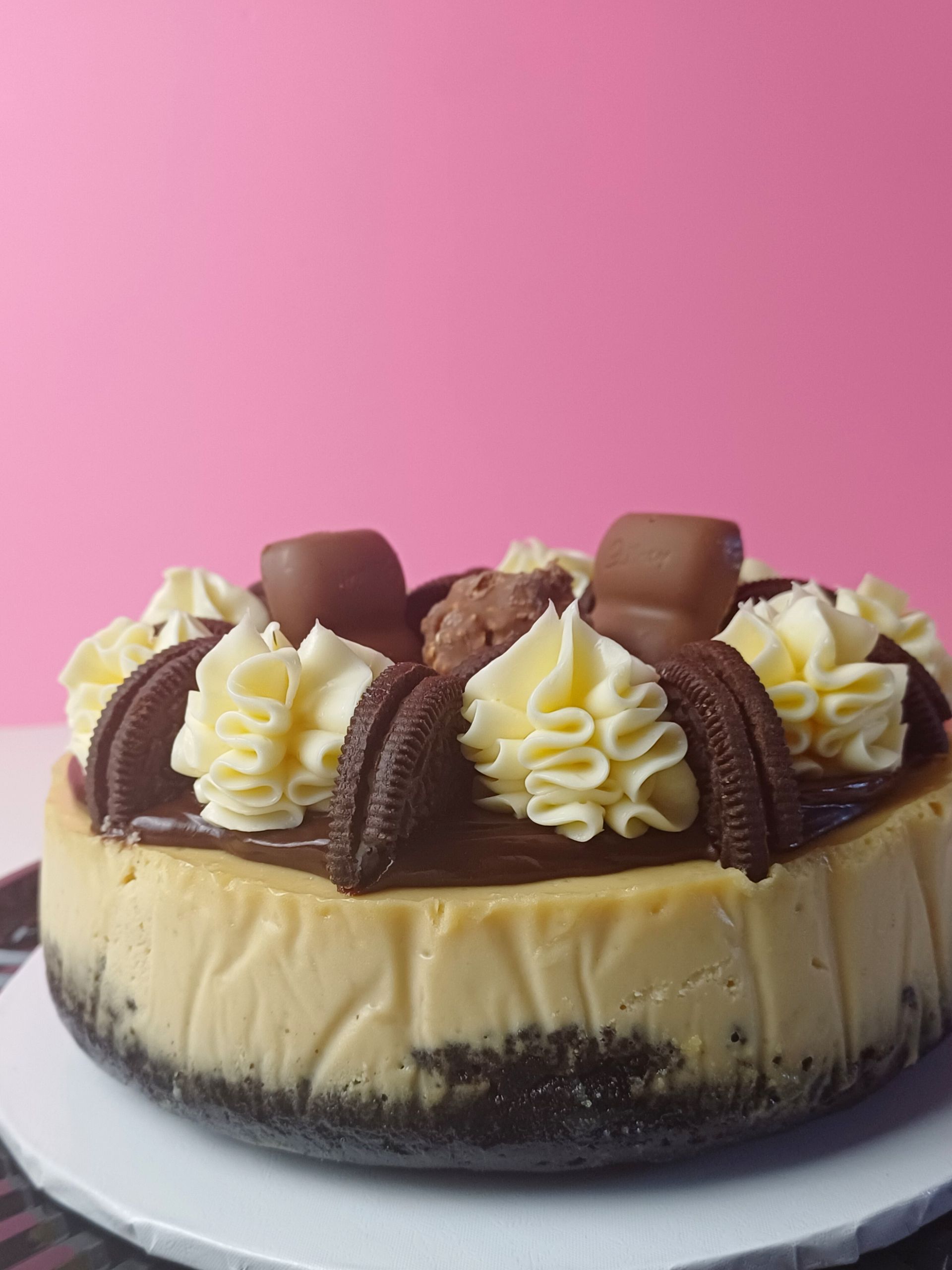 A decadent cheesecake with a chocolate cookie crust, topped with frosting swirls, chocolate sandwich cookies, and candy.
