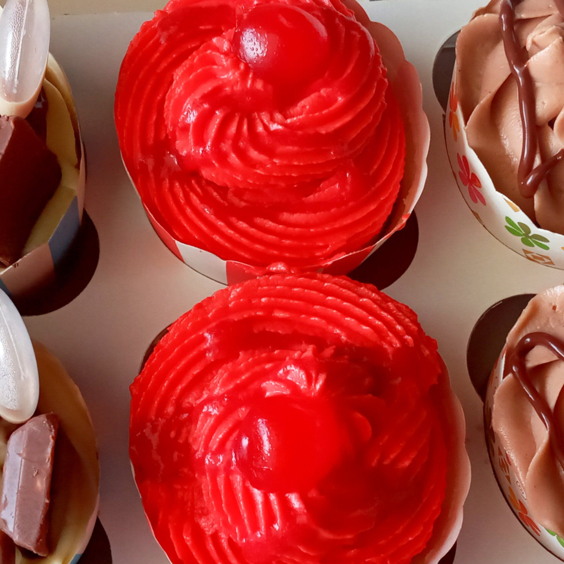 A box of cupcakes with red frosting and chocolate frosting