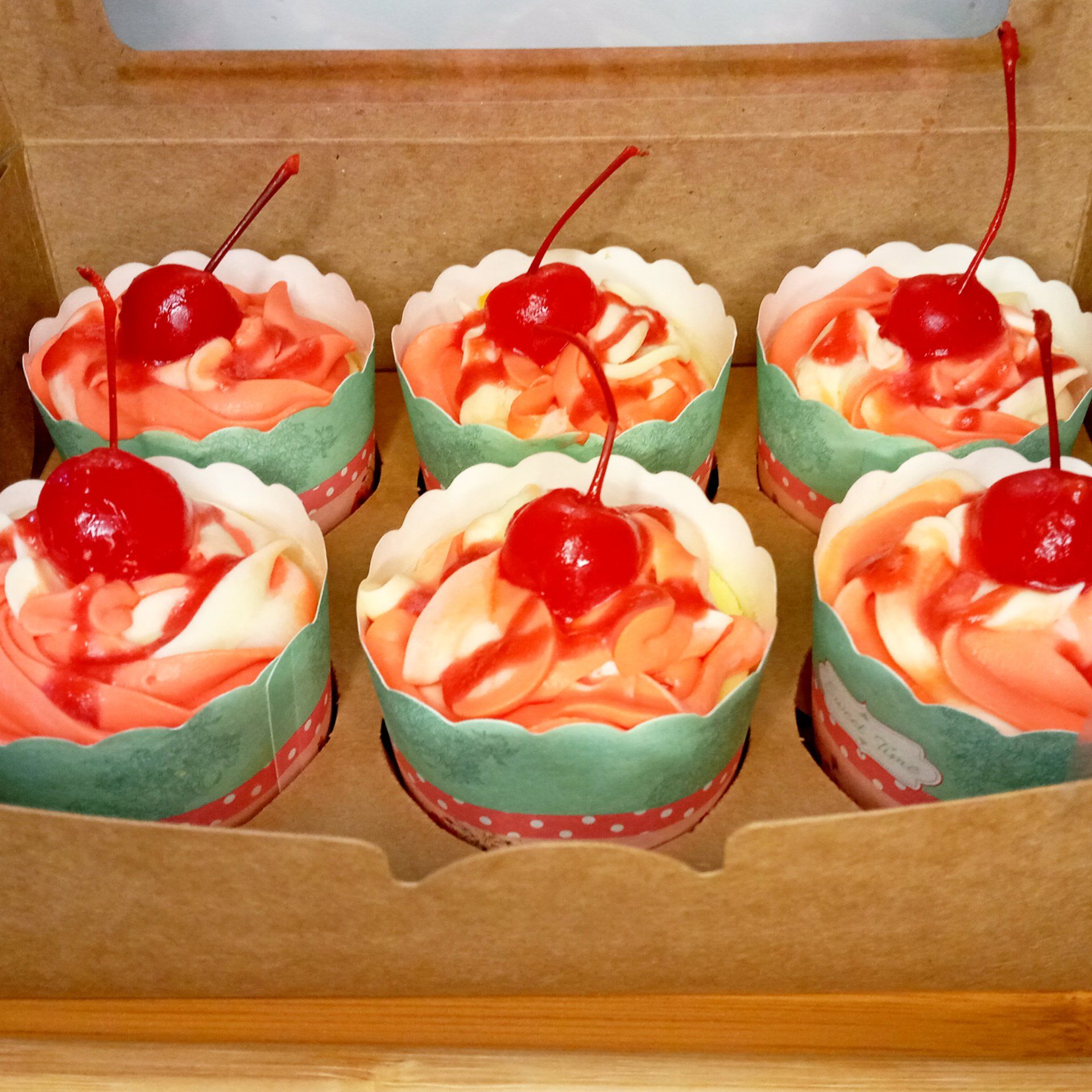 Six cupcakes in a box with cherries on top