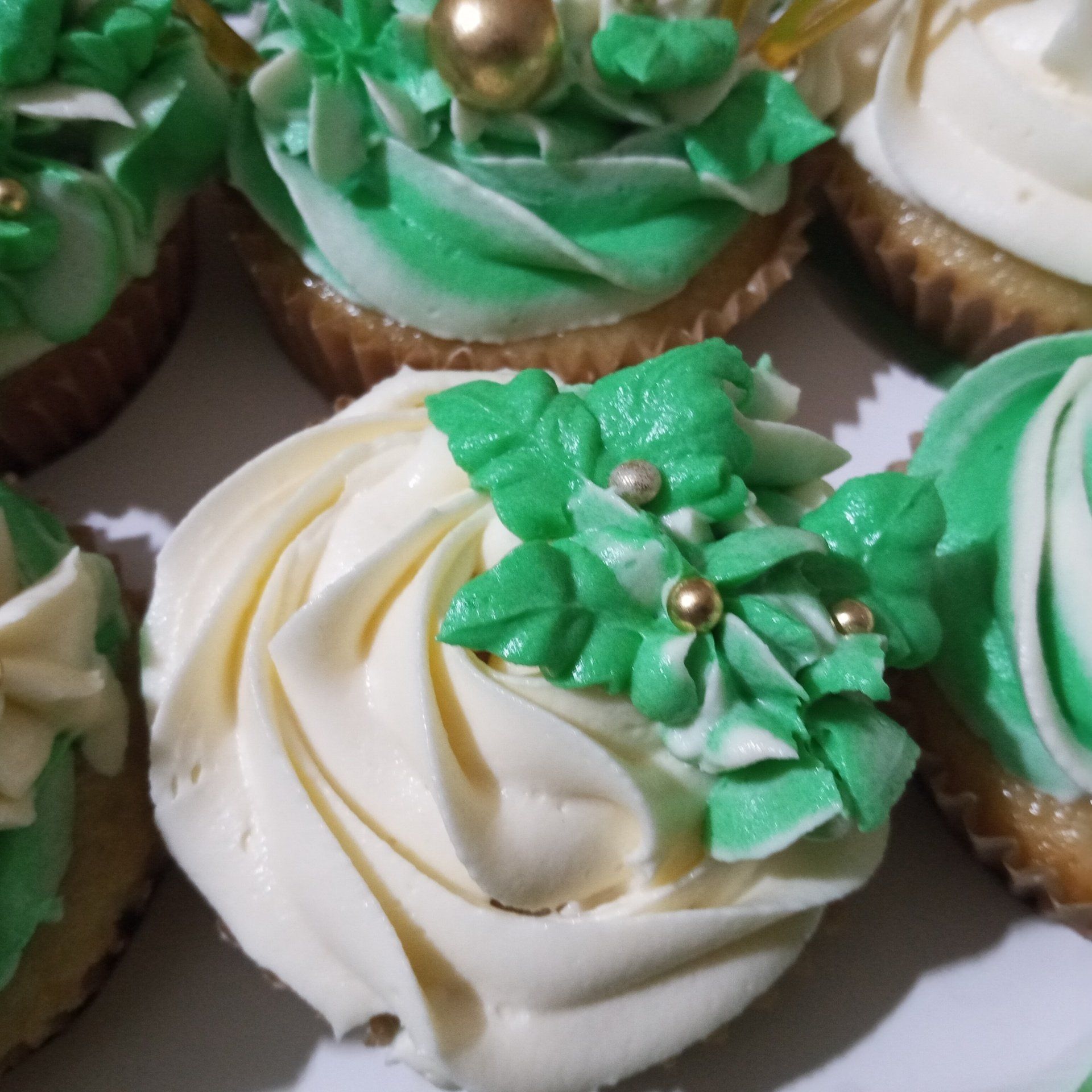 A bunch of cupcakes with green frosting and gold decorations