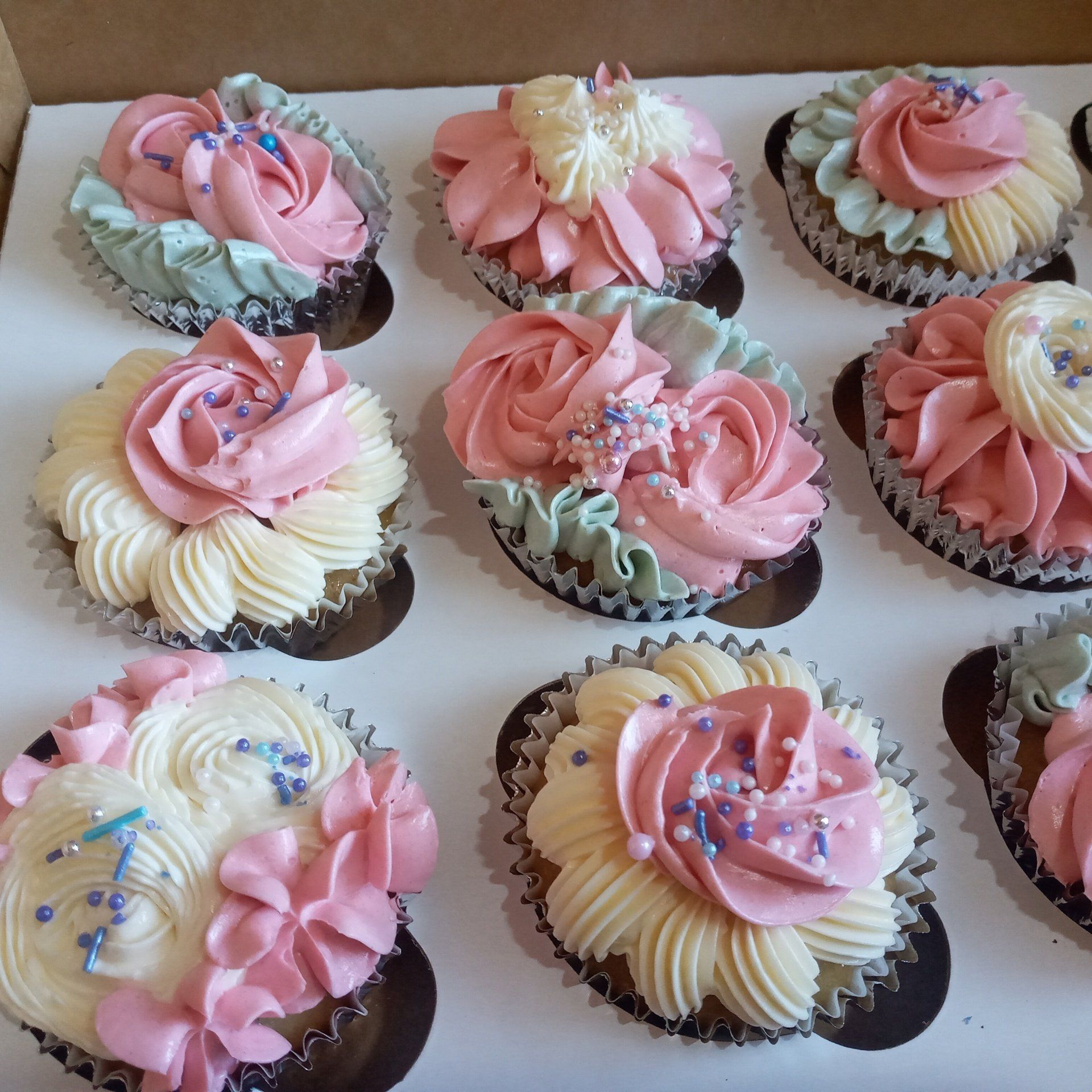 A box of cupcakes with pink and white frosting and sprinkles