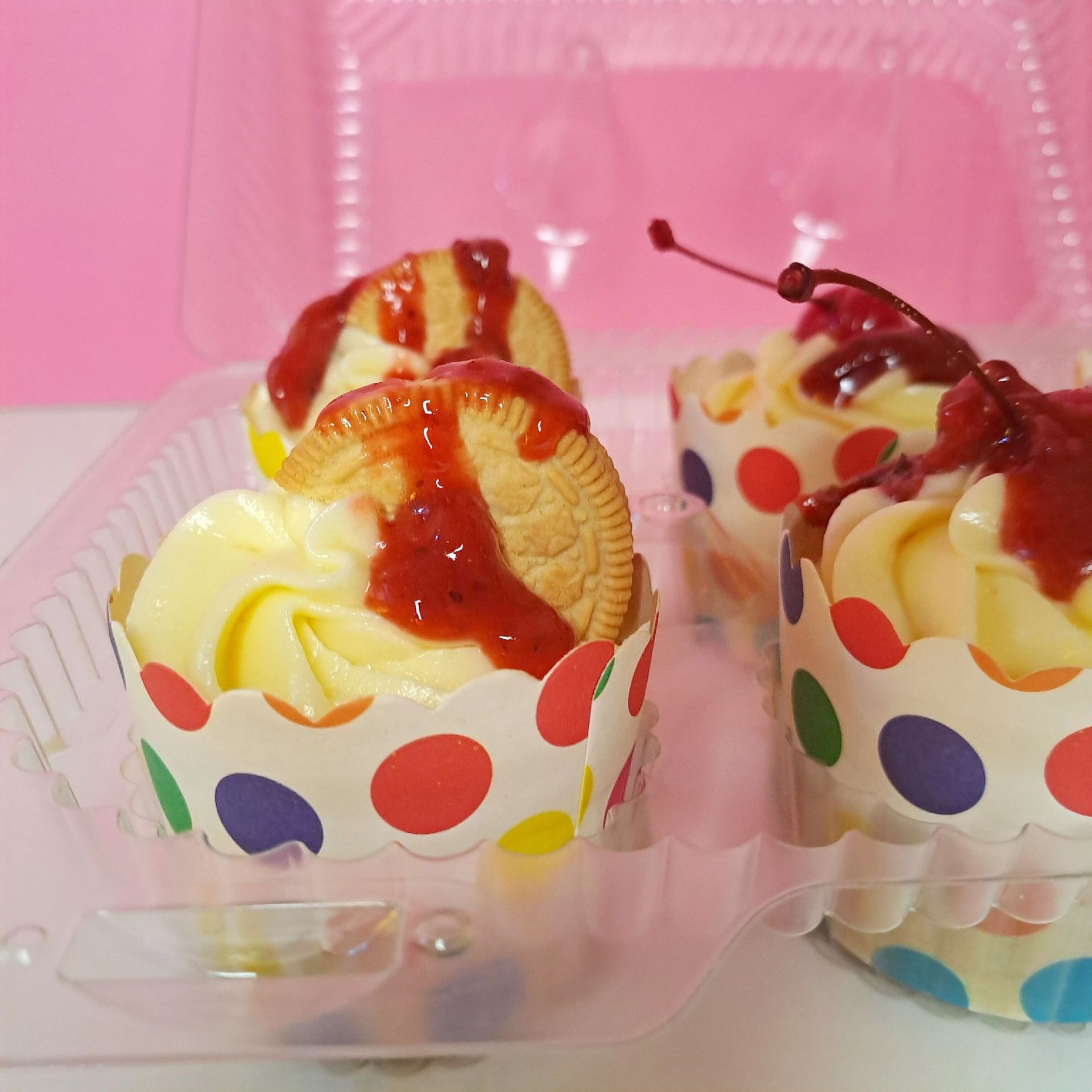 Three cupcakes in polka dot wrappers are in a plastic container