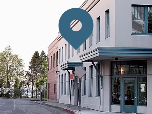 Blue map pin over a white and brick building on a street, indicating a location.