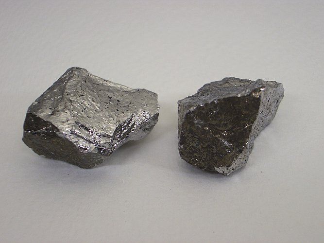 Two irregularly shaped, gray silicon chunks on a white surface.