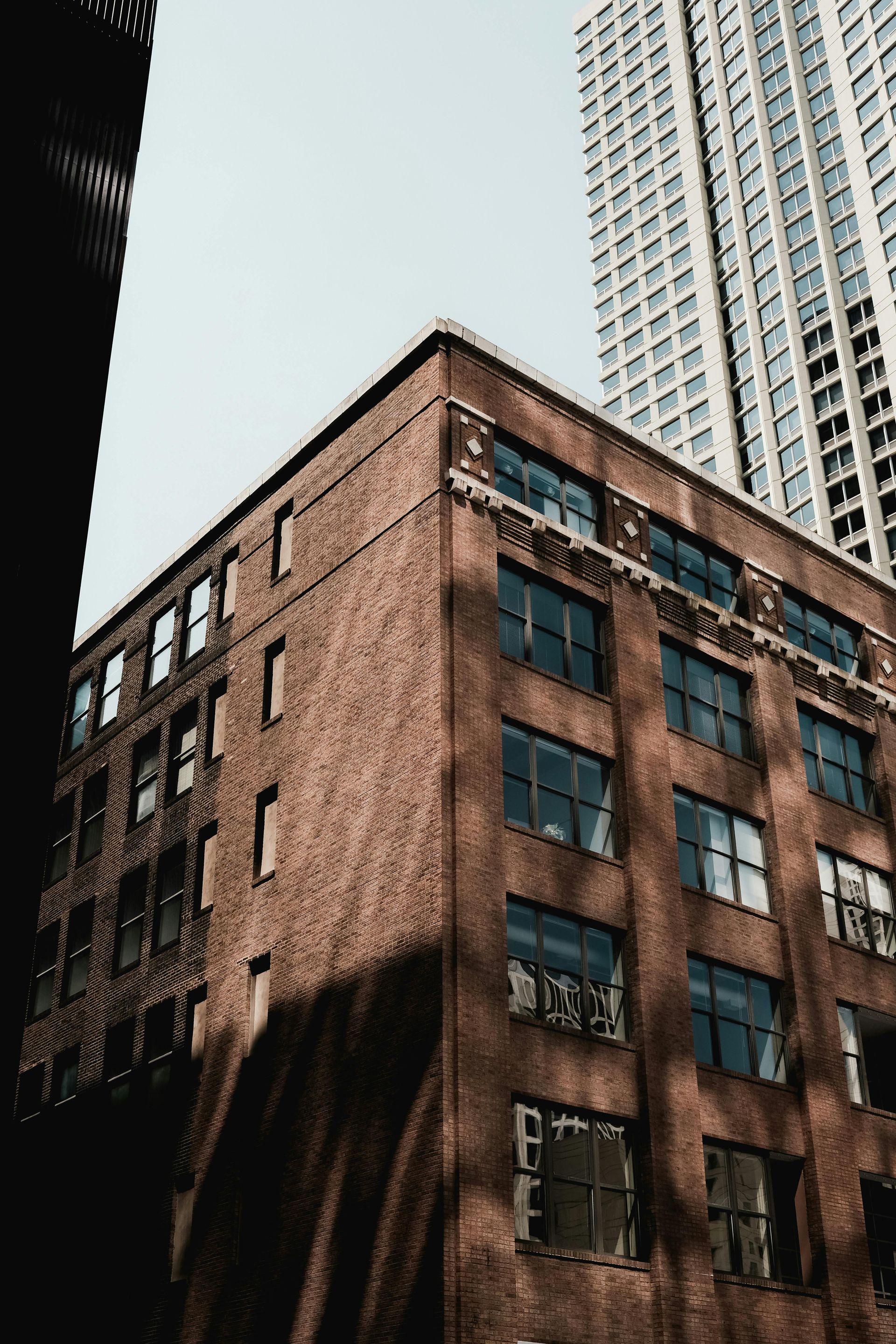 Brick building with multiple windows; tall skyscraper in the background. Sunny day.