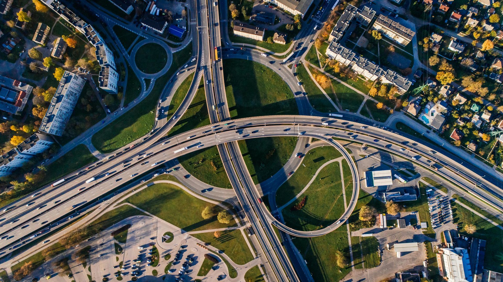 Overhead view of a multi-level highway interchange with heavy traffic, surrounded by buildings and greenery.